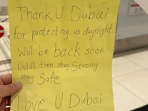 A small yellow paper with handwritten thank-you note and hearts held by a GDRFA officer at Dubai Airport.