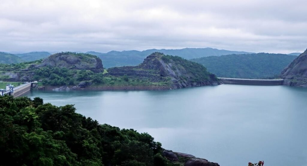 A wide-angle shot of the drying Idukki reservoir beds with the Arch dam in the background under a scorching sun.